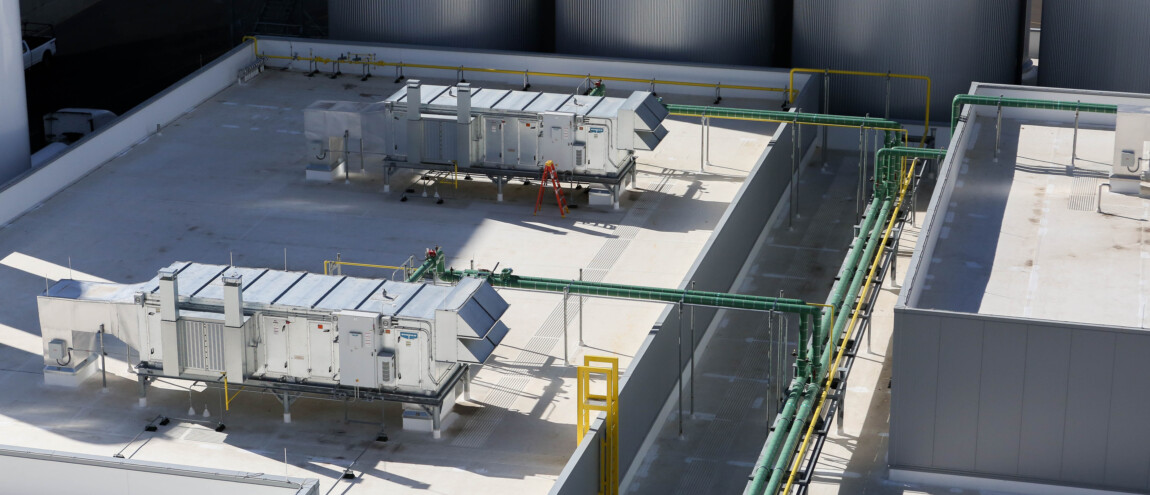 Industrial rooftop with HVAC units and green pipes.