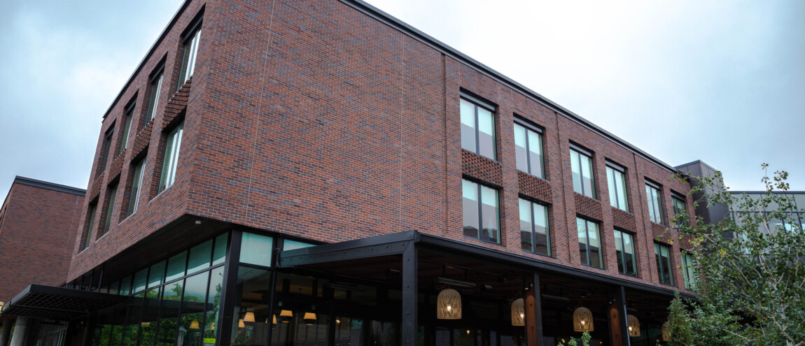 A modern brick building with large windows and greenery.