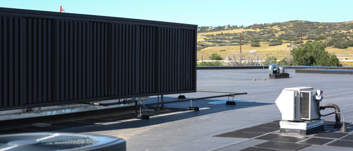 A large black air conditioner is positioned on a roof