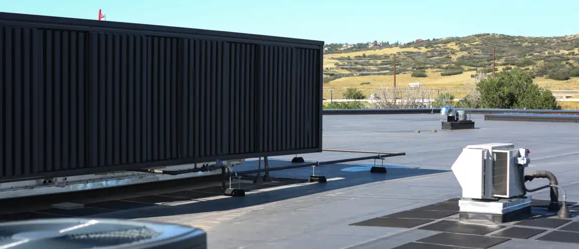 A large black air conditioner is positioned on a roof