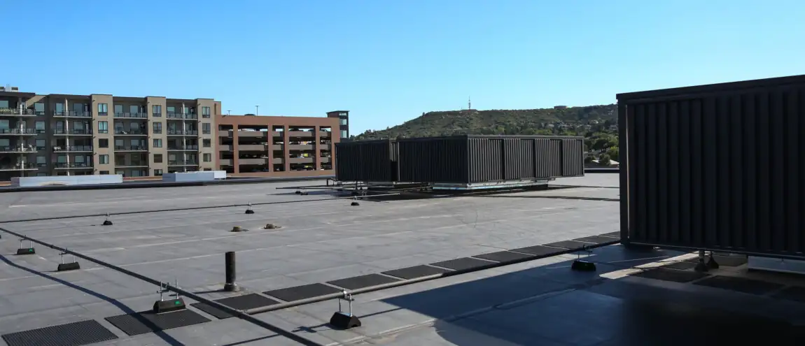 A large black air conditioner sits prominently on a rooftop against a clear blue sky.