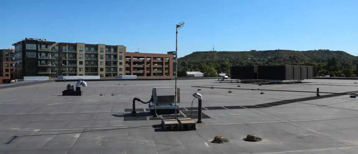 A flat roof in the foreground with a large building visible in the background against a clear sky.