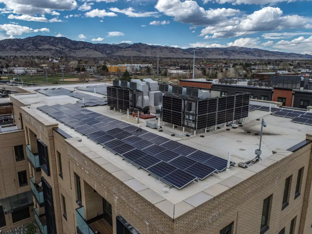 Rooftop solar panels with mountains and cloudy sky.