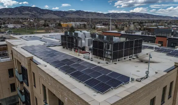 Rooftop solar panels with mountains and cloudy sky.