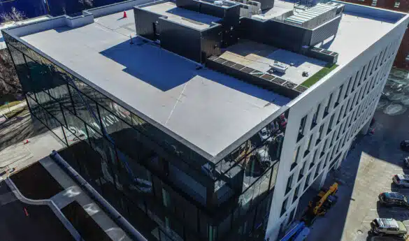 Aerial view of a modern five-story glass-and-concrete building, with construction vehicles and workers visible below