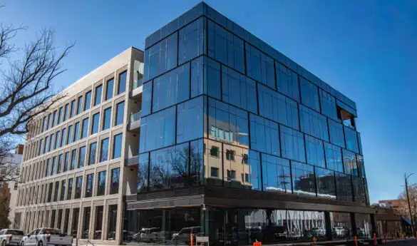 Modern office building with glass facade reflecting another structure, clear sky, and surrounding street elements